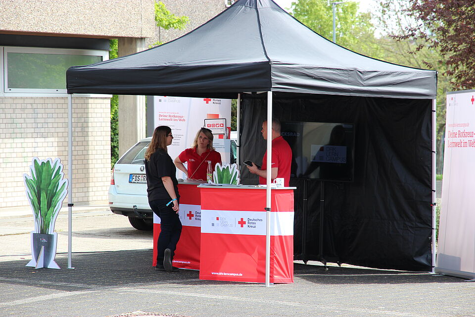 Zu sehen ist ein Pavillon des Deutschen Roten Kreuzes. Es unterhalten sich drei Personen miteinander